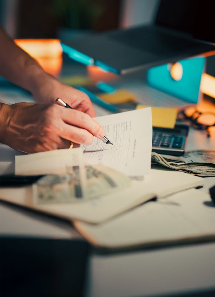 services-02 A hand signing financial documents on a desk with cash and a calculator, signifying finance management.